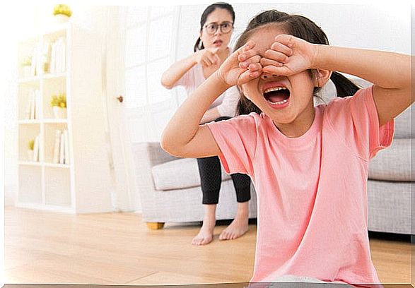 Little girl crying with her mother behind scolding.